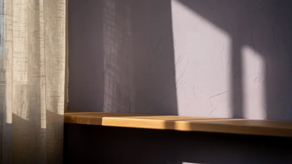 Late afternoon light through a linen curtain falling on a lilac plaster wall